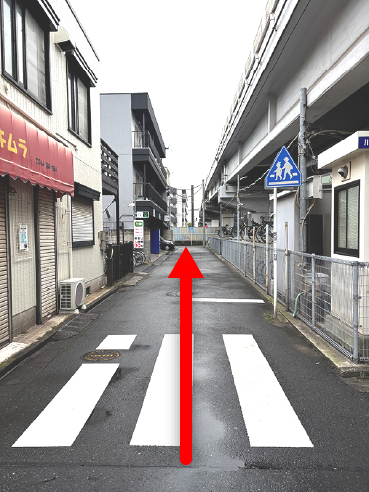 左手に赤い庇のお店がある、高架橋沿いの道の写真